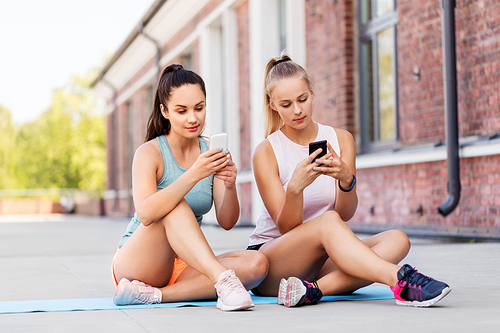 fitness, sport and healthy lifestyle concept - smiling young women or female friends with smartphone on rooftop