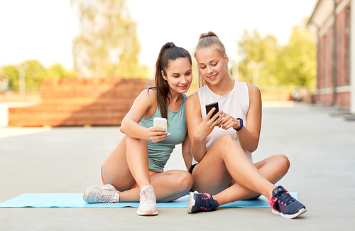 fitness, sport and healthy lifestyle concept - smiling young women or female friends with smartphones on rooftop