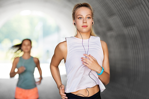 fitness, sport and healthy lifestyle concept - young women or female friends with earphones running outdoors