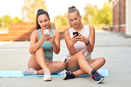 fitness, sport and healthy lifestyle concept - smiling young women or female friends with smartphones on rooftop