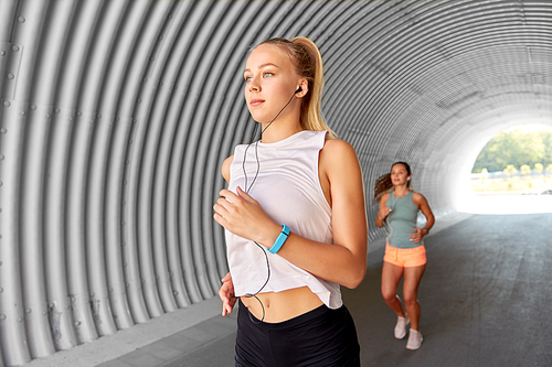 fitness, sport and healthy lifestyle concept - young women or female friends with earphones running outdoors