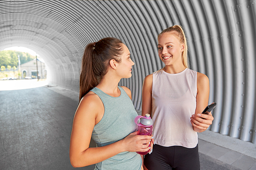 fitness, sport and healthy lifestyle concept - smiling young women or female friends with smartphone and flask