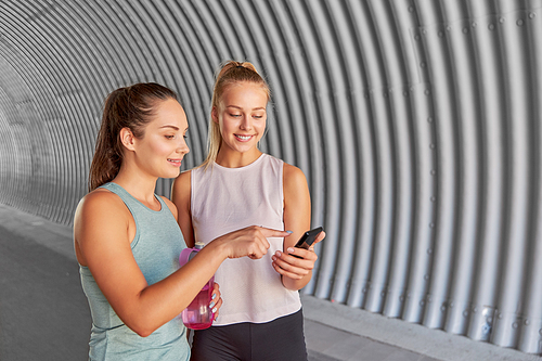 fitness, sport and healthy lifestyle concept - smiling young women or female friends with smartphone and flask