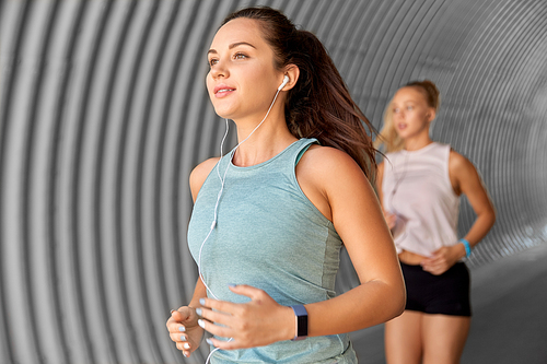 fitness, sport and healthy lifestyle concept - young women or female friends with earphones running outdoors