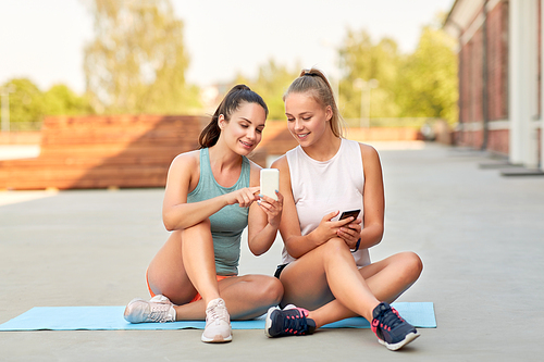 fitness, sport and healthy lifestyle concept - smiling young women or female friends with smartphones on rooftop