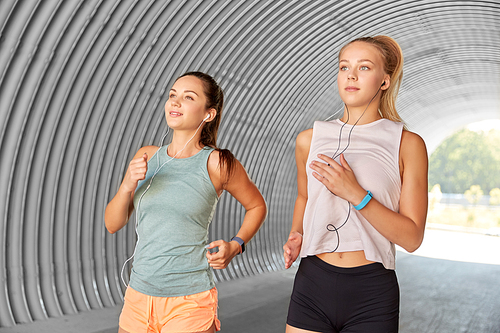 fitness, sport and healthy lifestyle concept - young women or female friends with earphones running outdoors