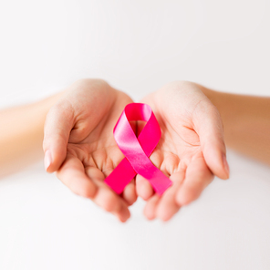 charity, healthcare and medicine concept - close up of woman cupped hands holding pink cancer awareness ribbon