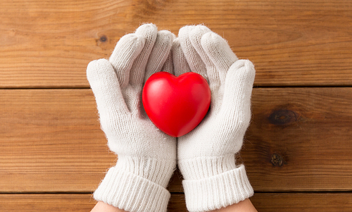 winter, valentine's day and christmas concept - hands in white woollen gloves holding red heart over wooden boards background