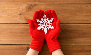 winter and christmas concept - hands in red woollen gloves holding big white snowflake over wooden boards background