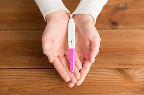 fertility and maternity concept - woman hands holding positive pregnancy test with two stripes over wooden boards background
