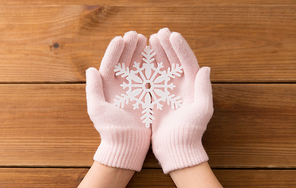 winter and christmas concept - hands in pale pink woollen gloves holding big white snowflake over wooden boards background
