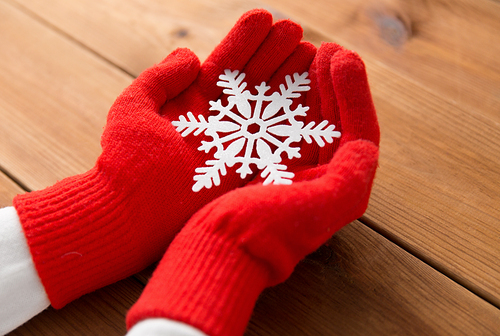 winter and christmas concept - hands in red woollen gloves holding big white snowflake over wooden boards background