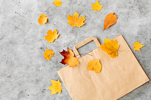 shopping and mid season sale concept - autumn leaves and paper bag on grey stone background
