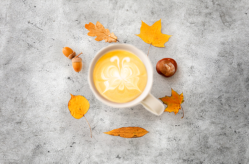 drinks, season and latte art concept - cup of coffee with butterfly on foam, autumn leaves, acorns and chestnut on grey stone background