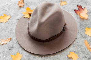 season, headwear and clothes concept - hat and fallen autumn leaves on gray stone background