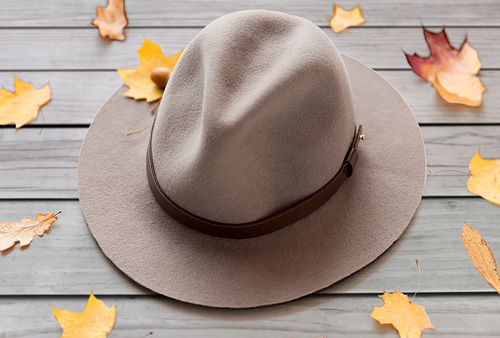 season, headwear and clothes concept - hat and fallen autumn leaves on gray wooden boards background