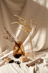 packing and decoration concept - still life of gift box, craft wrapping paper, rope and scissors with dried flowers in vases on drapery