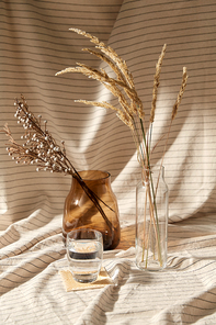 home improvement and decoration concept - still life of water in glass, decorative dried flowers in vase and bottle over drapery