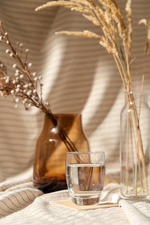 home improvement and decoration concept - still life of water in glass, decorative dried flowers in vase and bottle over drapery