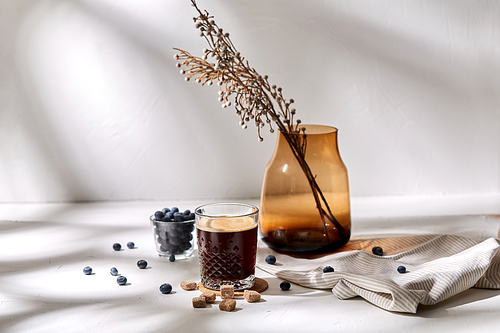 objects and drinks concept - glass of coffee on cork drink coaster, brown sugar, blueberries and vase with dried flowers on table
