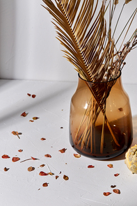 home improvement and decoration concept - still life of decorative dried flowers in brown glass vase and petals