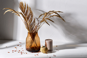 home improvement and decoration concept - still life of decorative dried flowers in brown glass vase, candle and pumpkin