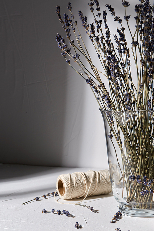 packing and decoration concept - still life of dried lavender flowers in glass vase, craft rope dropping shadows on white surface