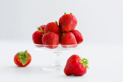 fruit, food and berries concept - strawberries on glass stand over white background