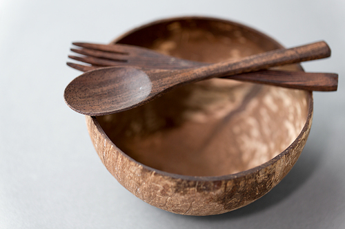 recycling, tableware and eco friendly concept - close up of coconut bowl with brown wooden spoon and fork on table