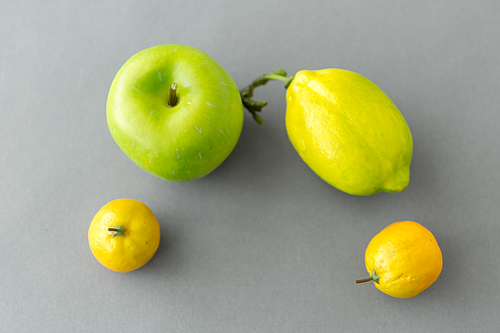 food, fruit and healthy eating concept - close up of green apple and lemons on grey