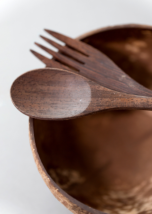 recycling, tableware and eco friendly concept - close up of coconut bowl with brown wooden spoon and fork on table
