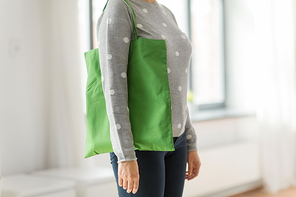 consumerism and eco friendly concept - woman with green reusable canvas bag for food shopping on grey background