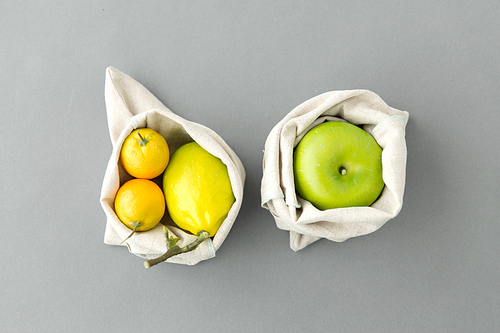 consumerism and  friendly concept - fruits in reusable canvas bags for food shopping s on grey background