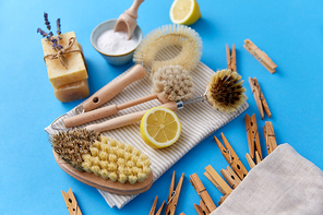 natural cleaning stuff, sustainability and eco living concept - different brushes, lemon, wooden clothespins and washing soda with soap on blue background