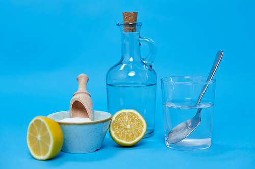 natural cleaning stuff, sustainability and eco living concept - lemon halves, washing soda, bottle of vinegar and glass with spoon over blue background