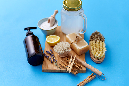 natural cleaning stuff and eco living concept - washing soda, laundry and liquid soap, wooden clothespins, with brushes and lemon on blue background