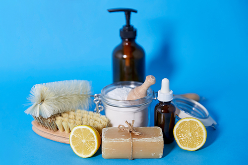 natural cleaning stuff, sustainability and eco living concept - lemon halves, washing soda, bottle of vinegar with laundry and liquid soap and brushes on blue background