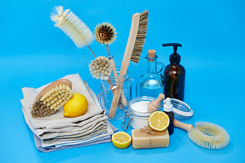 natural cleaning stuff, sustainability and eco living concept - lemon halves, washing soda, bottle of vinegar with laundry and liquid soap and brushes on blue background
