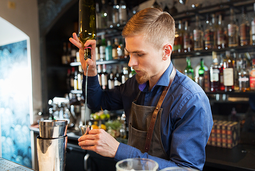 drinks, people and luxury concept - barman with shaker pouring alcohol from bottle into jigger and preparing cocktail at bar