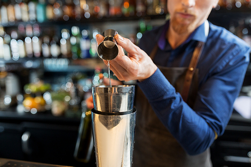 drinks, people and luxury concept - barman pouring alcohol from jigger into shaker and preparing cocktail at bar