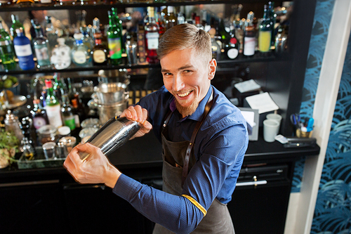 alcohol drinks, people and luxury concept - happy smiling barman with shaker preparing cocktail at bar