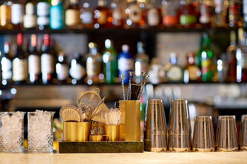 alcohol drinks, equipment and luxury concept - shakers, glasses with ice, stirrers and strainers on bar counter