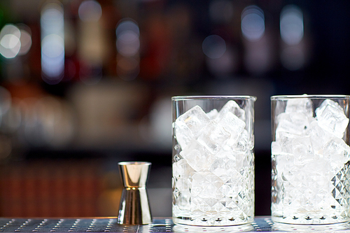 alcohol drinks and luxury concept - two vintage glasses with ice cubes and jigger on bar counter