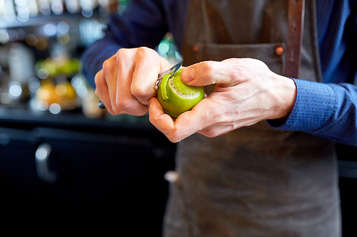 people and profession concept - bartender with peeler removing peel from lime at bar