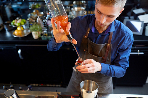 drinks, people and luxury concept - bartender with shaker pouring alcohol from bottle into jigger and preparing cocktail at bar
