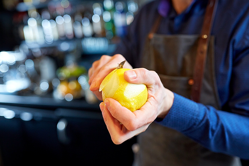 people and profession concept - bartender with peeler removing peel from lemon at bar