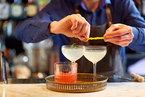 alcohol drinks, people and luxury concept - bartender with glasses and lemon peel preparing cocktail at bar