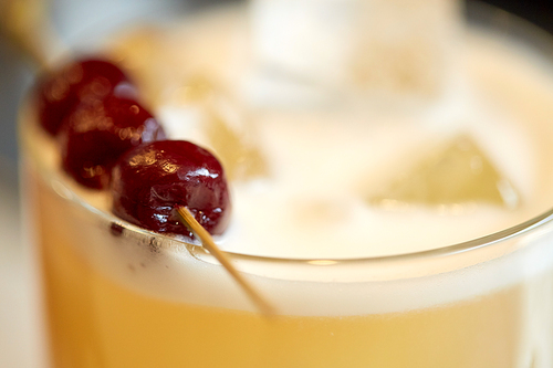 alcohol drinks and luxury concept - close up of cocktail glass with cherries at bar
