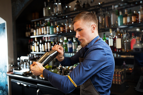 alcohol drinks, people and luxury concept - barman with shaker preparing cocktail at bar