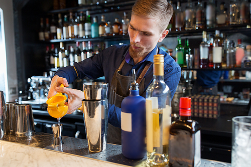 alcohol drinks, people and luxury concept - barman with shaker and bottles squeezing juice into jigger and preparing cocktail at bar